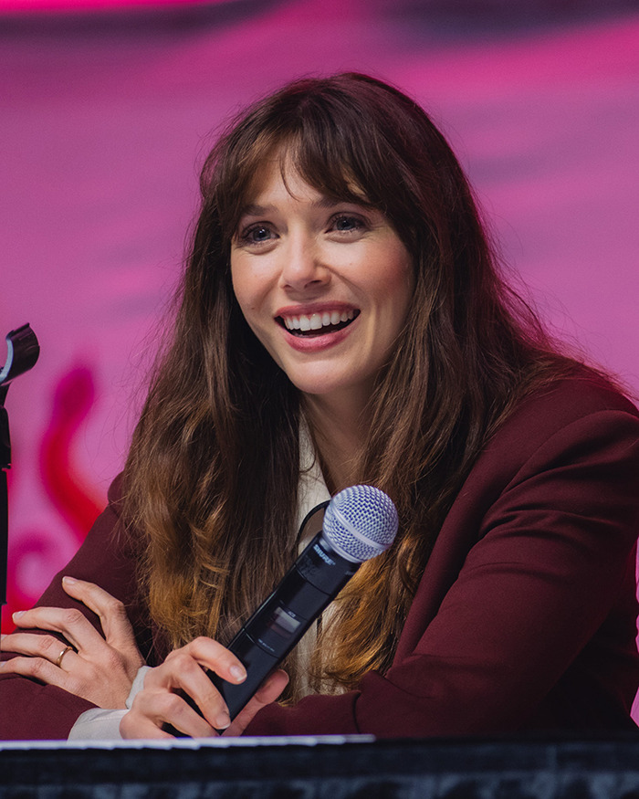 Elizabeth Olsen speaking at a panel, holding a microphone, breaking down the viral 6,7 meme with a smile. Elizabeth Olsen speaking at a panel, holding a microphone, breaking down the viral 6,7 meme with a smile.