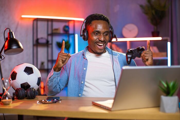 Man wearing headphones and holding game controller excitedly gaming on laptop, illustrating craziest coincidences.