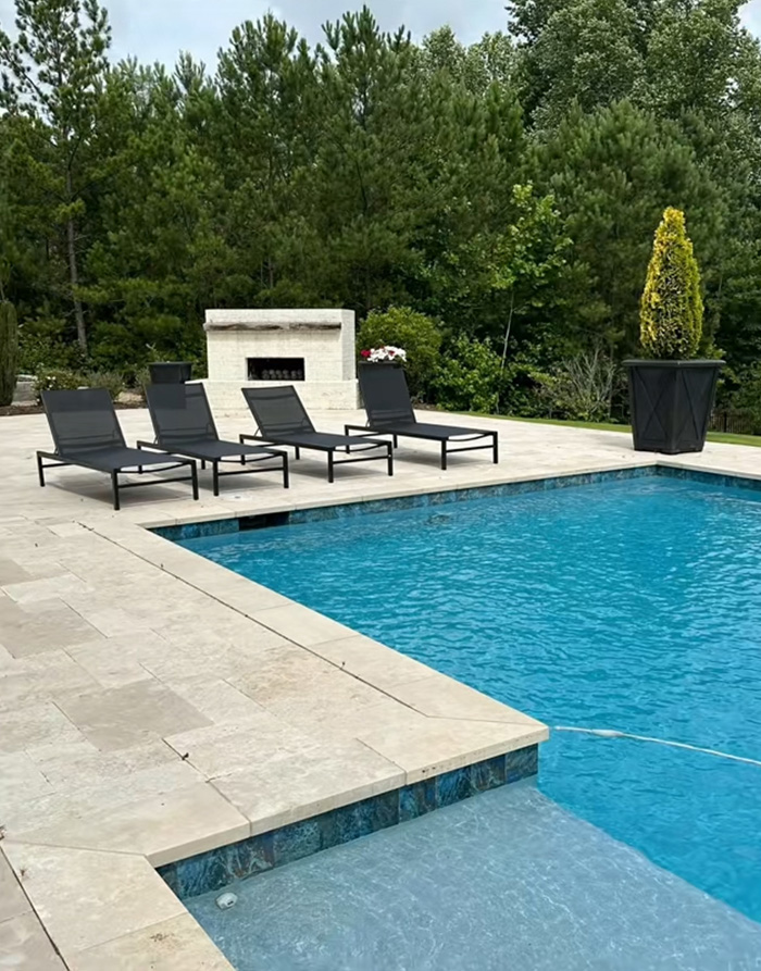Swimming pool with black lounge chairs and trees in the background, reflecting tree law and neighbor dispute concepts.