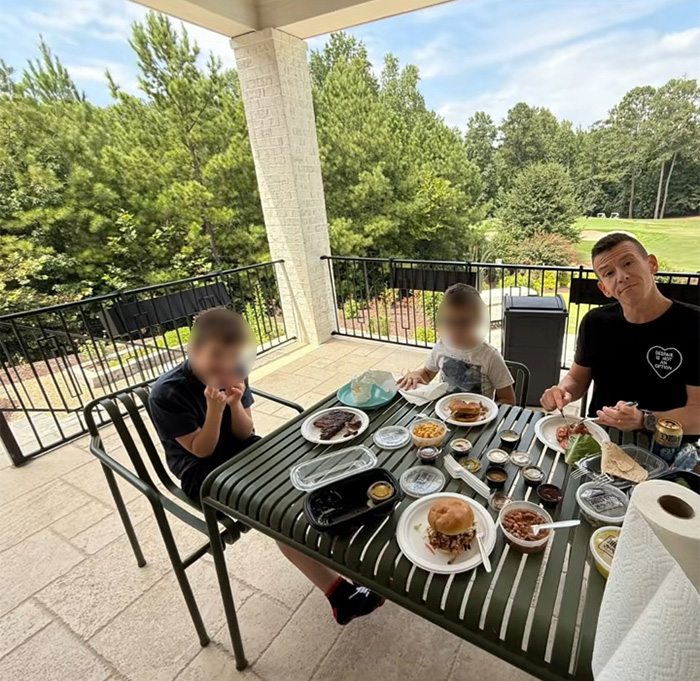 Family having outdoor meal on patio near trees, highlighting tree law debate after neighbor bulldozed all trees.