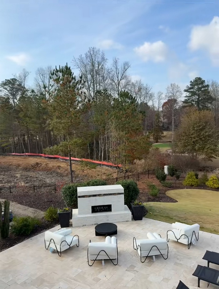 Outdoor patio with white chairs and fireplace overlooking area where trees were bulldozed sparking tree law debate. Outdoor patio with white chairs and fireplace overlooking area where trees were bulldozed sparking tree law debate.