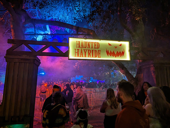 Crowd waiting under a glowing haunted hayride sign with spooky lighting and fog at a nighttime event. Crowd waiting under a glowing haunted hayride sign with spooky lighting and fog at a nighttime event.