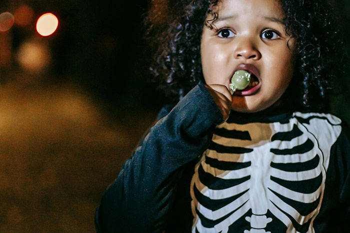 Child in skeleton costume eating candy, looking scared while on a haunted hayride with parents. Child in skeleton costume eating candy, looking scared while on a haunted hayride with parents.