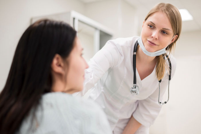 Female ER staff wearing a stethoscope attentively speaking to a patient in a hospital setting demonstrating care and authority. Female ER staff wearing a stethoscope attentively speaking to a patient in a hospital setting demonstrating care and authority.