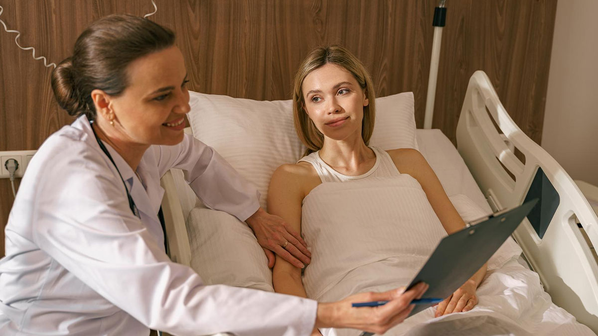 Female patient in hospital bed listens to female ER staff explaining medical information on clipboard