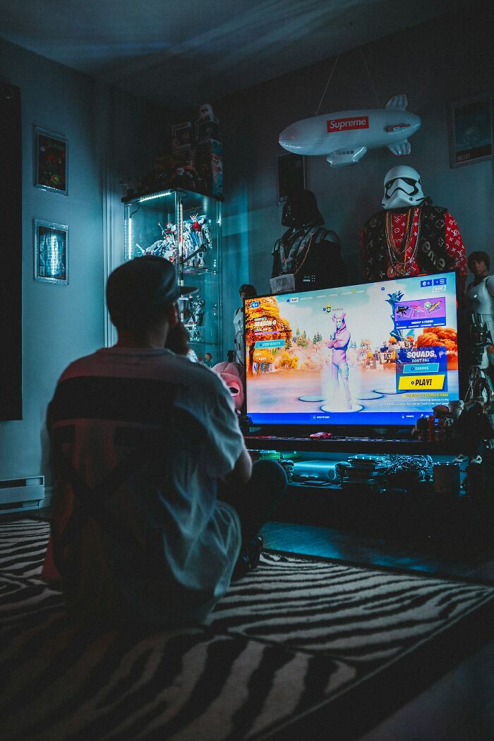 Person playing video games in a dim room surrounded by collectibles, reflecting themes of love and friendship destroyed by broken trust.