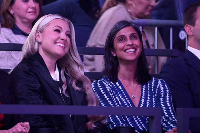 Erika Kirk smiling and seated next to a woman in a blue patterned dress during a public event.