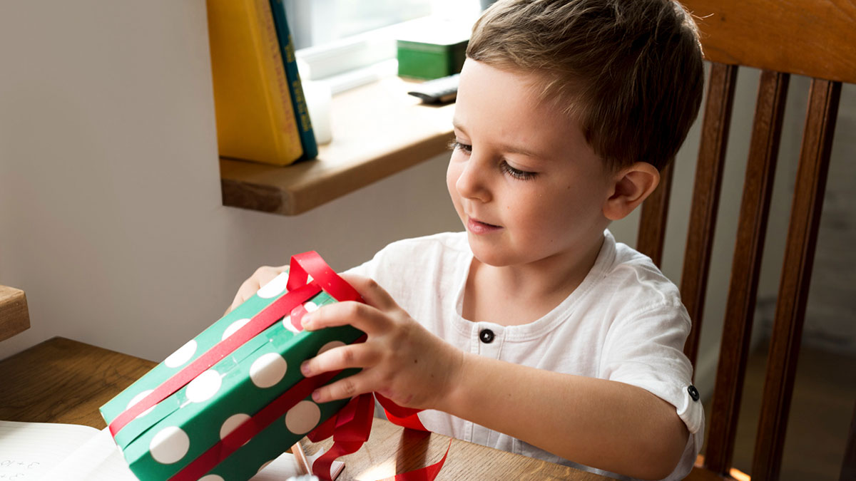Young boy opening a wrapped gift at home, hinting at AirPods given by ex-husband that are traceable concerns for mom.