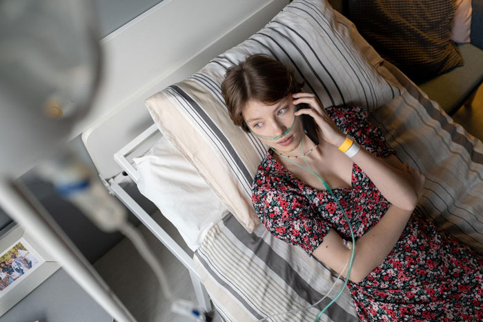 Young woman with oxygen tube lying in hospital bed talking on phone, illustrating terminally ill patient scenario. Young woman with oxygen tube lying in hospital bed talking on phone, illustrating terminally ill patient scenario.