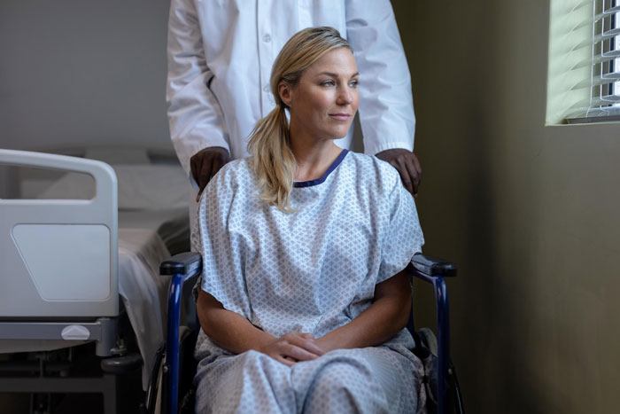 Woman in hospital gown sitting in wheelchair, man standing behind her, reflecting a man refusing to visit terminally ill ex-GF. Woman in hospital gown sitting in wheelchair, man standing behind her, reflecting a man refusing to visit terminally ill ex-GF.