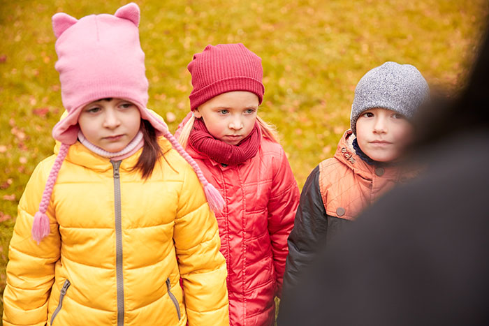 Three children in winter jackets and hats look serious and distant outdoors on a chilly autumn day. Three children in winter jackets and hats look serious and distant outdoors on a chilly autumn day.