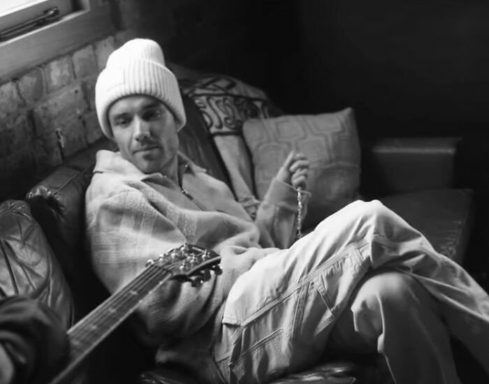 Man in a beanie and casual clothing sitting on a leather couch, holding a string of beads, related to Simon Cowell and Liam Payne. Man in a beanie and casual clothing sitting on a leather couch, holding a string of beads, related to Simon Cowell and Liam Payne.