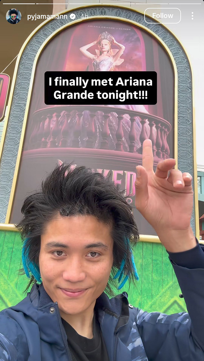Young man with blue-tipped hair posing in front of promotional poster referencing Ariana Grande at a premiere event. Young man with blue-tipped hair posing in front of promotional poster referencing Ariana Grande at a premiere event.