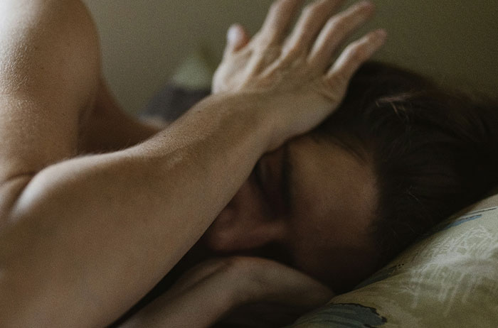 Woman in bed with hand on forehead, appearing distressed, illustrating unexpected life endings and emotional struggle.