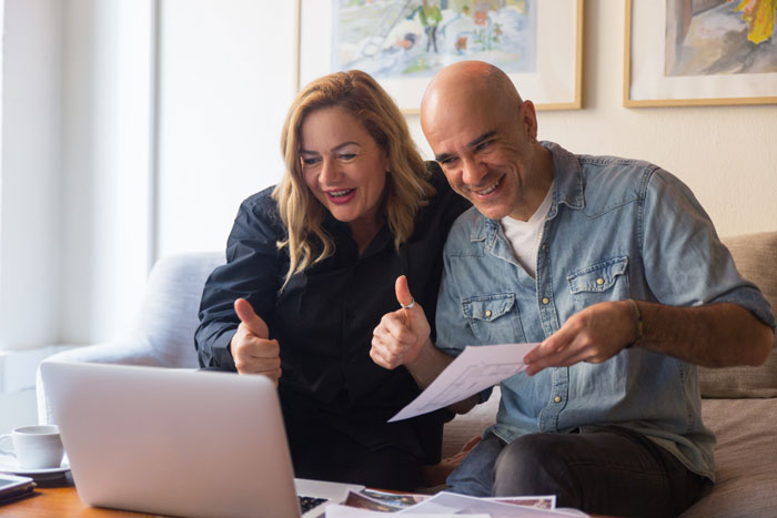 Man and woman smiling and giving thumbs up while discussing documents on a laptop about charging daughter $15K for raising her