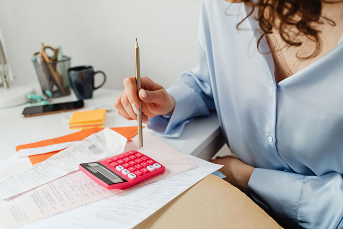 Woman calculating expenses with a calculator and documents, concerned about charges related to raising a minor daughter.