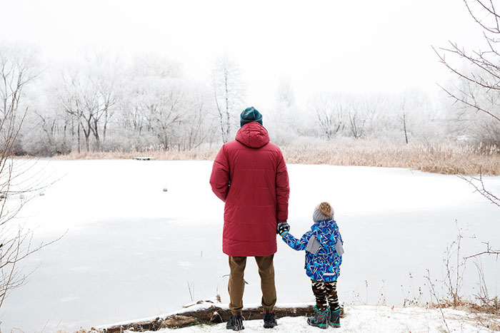Man in red coat holding child’s hand by frozen lake in winter, illustrating selfish dad demands apology from daughter story.