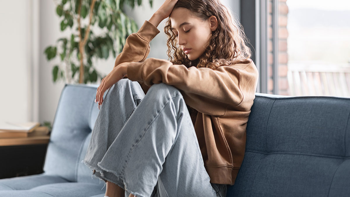 Sad young woman sitting on couch with head in hand, reflecting on ruined Christmas memory and selfish dad conflict.
