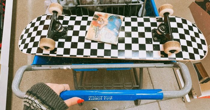 Checkered skateboard and vintage comic book in shopping cart, highlighting a unique thrift find by a shopper.
