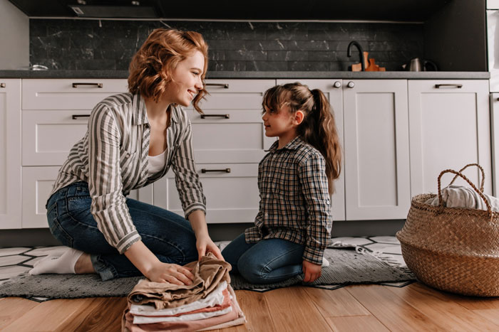 Young woman babysitting daughter in kitchen, folding clothes together, bonding during a calm home moment. Young woman babysitting daughter in kitchen, folding clothes together, bonding during a calm home moment.