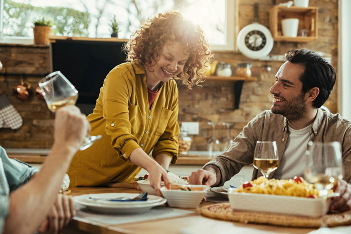 Childfree couple sharing a meal in a warm kitchen setting, with a woman smiling and serving food to a man.