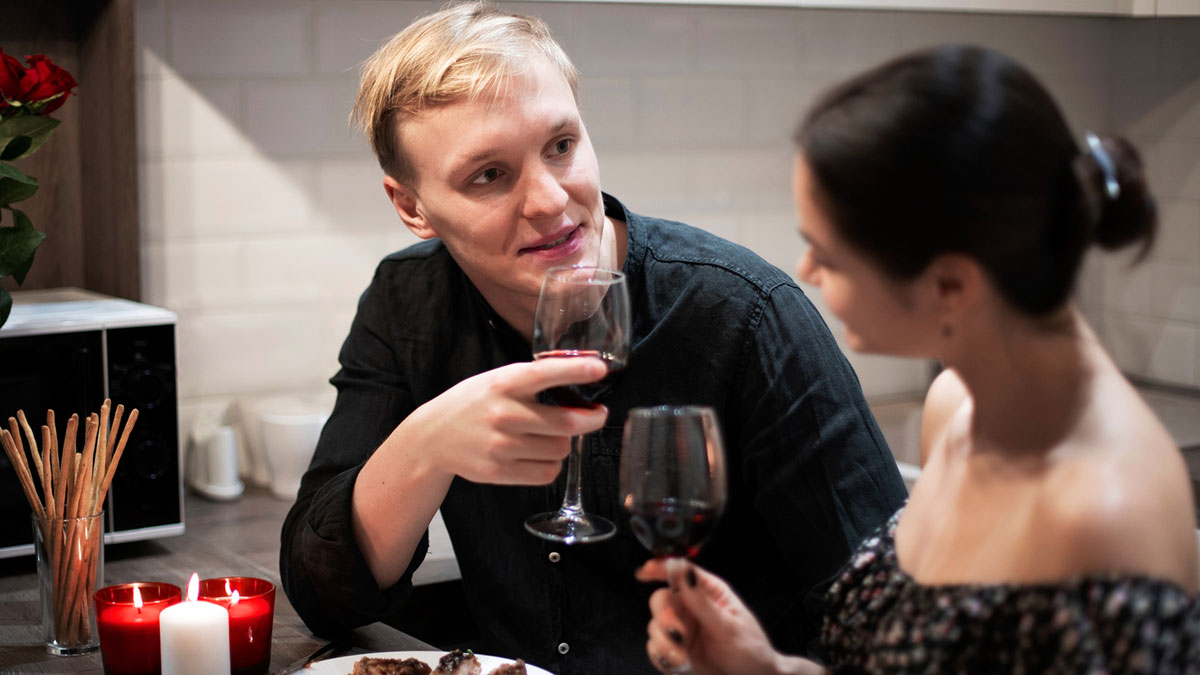 Childfree couple in conflict sharing tense dinner with red wine and lit candles in cozy kitchen setting.