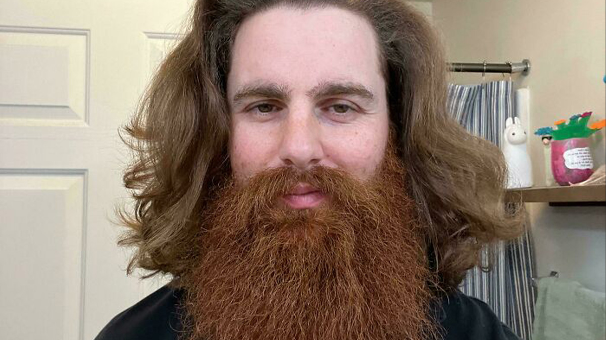 Man with fierceflow long hair and full thick beard posing indoors in a casual setting with bathroom background.