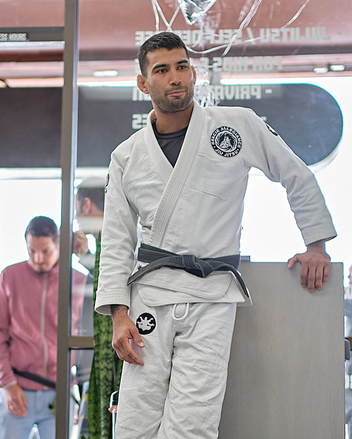 Jiu-Jitsu trainer in white gi with black belt standing inside gym after tragic freak accident sparring incident. Jiu-Jitsu trainer in white gi with black belt standing inside gym after tragic freak accident sparring incident.