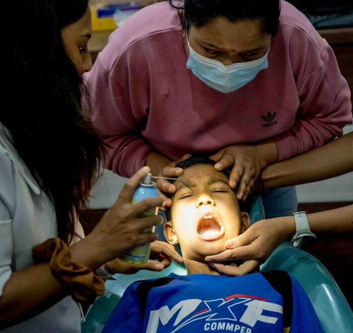 Dentist treating a young patient with multiple hands assisting during a dental procedure under bright light.