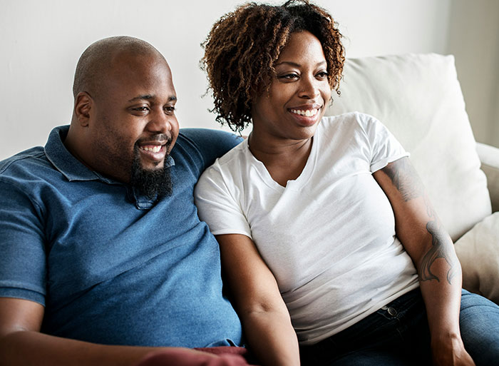 Couple sitting closely on a couch smiling, illustrating friendship crumbles after woman exposes friend’s secret.