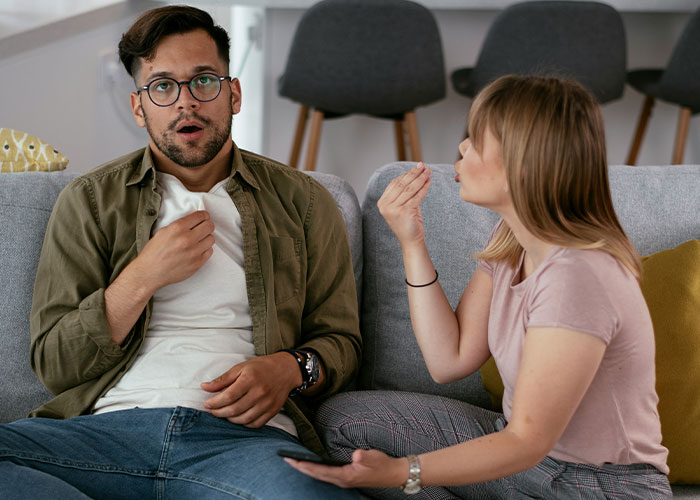Man looking shocked while woman angrily confronts him on a couch, illustrating friendship crumbles after secret exposed. Man looking shocked while woman angrily confronts him on a couch, illustrating friendship crumbles after secret exposed.