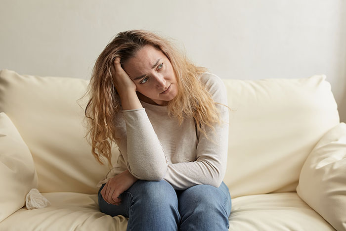 Woman sitting on couch looking stressed and contemplative, reflecting on clingy children and vacation struggles. Woman sitting on couch looking stressed and contemplative, reflecting on clingy children and vacation struggles.