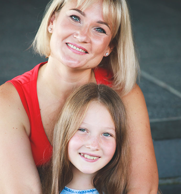 Smiling woman and her daughter sitting closely together, illustrating clingy children and family vacation challenges. Smiling woman and her daughter sitting closely together, illustrating clingy children and family vacation challenges.