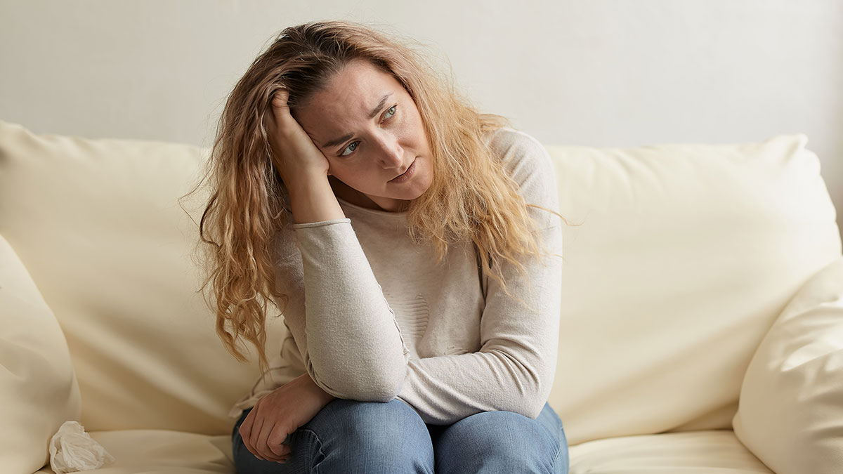 Woman with long curly hair sitting on a couch looking upset, illustrating conflict about clingy children on vacation.