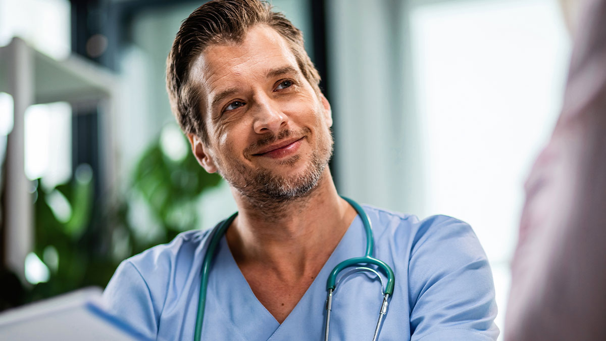 Smiling male doctor in scrubs with stethoscope, creating a lighthearted vibe in hospitals and clinics with patients.