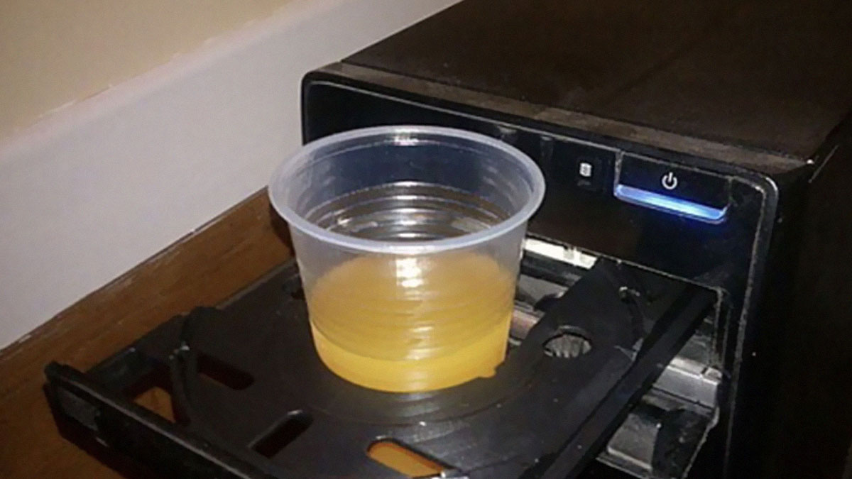 Plastic cup with orange juice placed in a CD drive slot of a desktop computer, a funny Wikipedia gem found online.