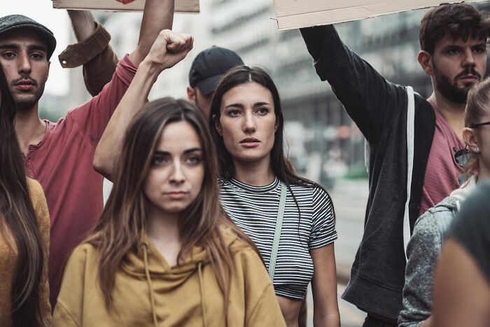 A group of diverse young people in a protest holding signs, highlighting upcoming events to pay attention to online.