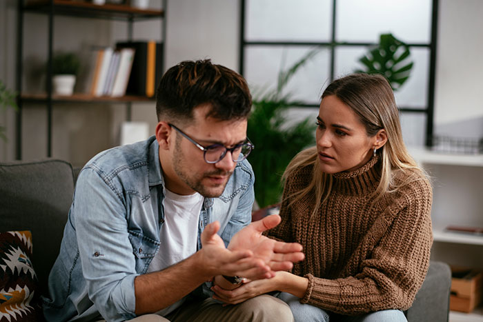 Man and woman having a serious conversation on couch, illustrating family conflict and relationship wedge issues.