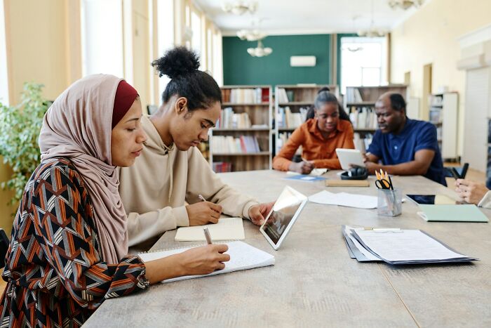 Group of diverse young adults working and discussing ideas together in a library setting, highlighting funny moments with loved ones.