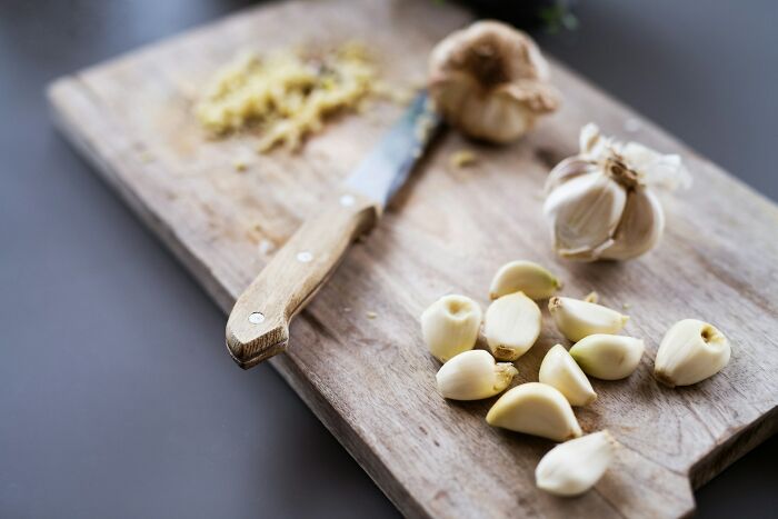 Knife with wooden handle on a cutting board next to peeled garlic cloves, highlighting sharpen your knives for cooking.