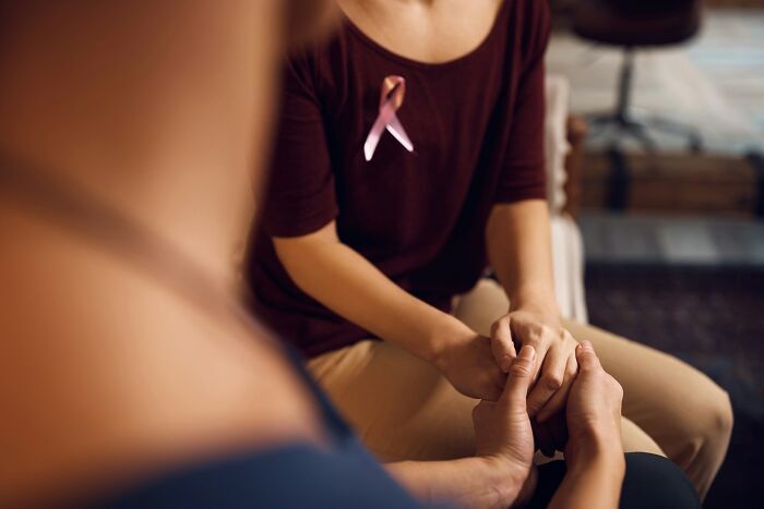 Person wearing a cancer awareness ribbon holding hands with another, symbolizing support during a hard time.