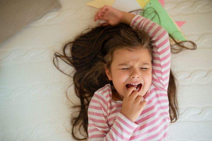 Young girl in striped shirt lying on bed with a frustrated expression, capturing funny and serious moments of parenting challenges.
