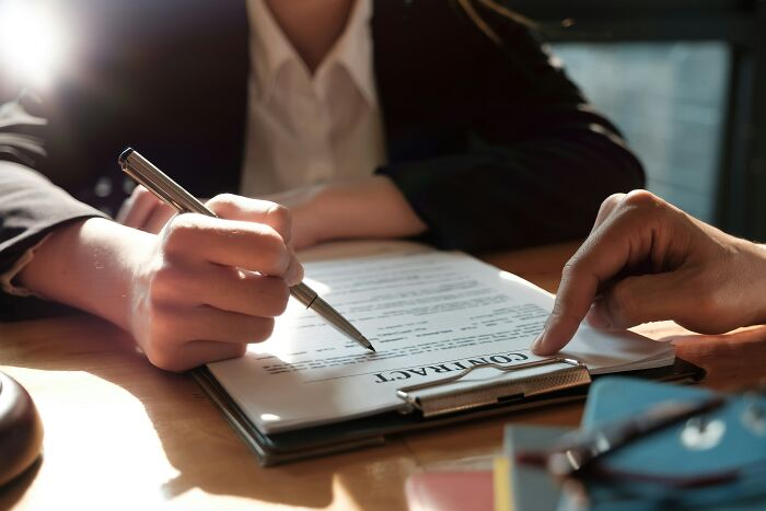 Two professionals reviewing and signing a contract at work, illustrating infuriating workplace traditions.