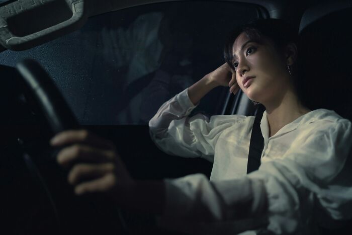 Young woman sitting in a car at night, looking worried and tense, capturing a real-life horror story moment.