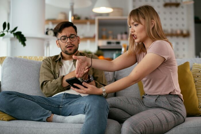 Couple arguing on a couch, woman showing phone to man, depicting broken trust in love and friendship.