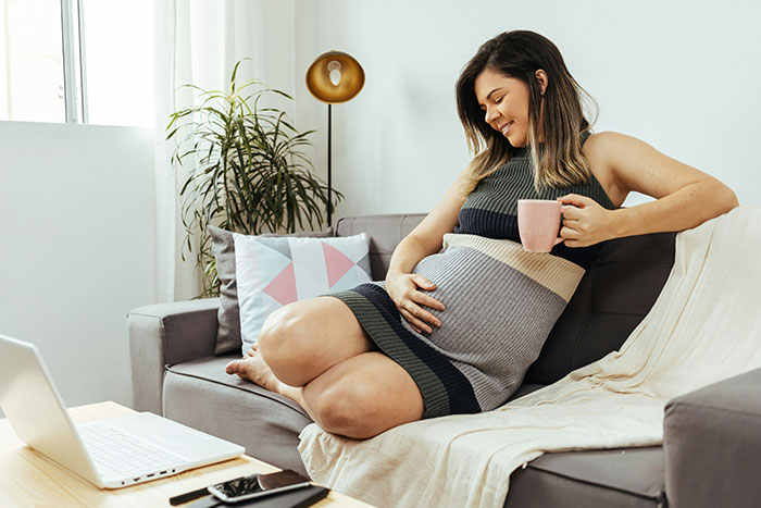 Pregnant woman relaxing on sofa with coffee, gently holding belly, representing pregnant woman demand husband respect concept.