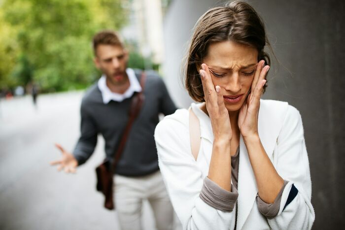 Woman upset holding her face while man in background argues on a city street, depicting awkward wedding moments and crashes.