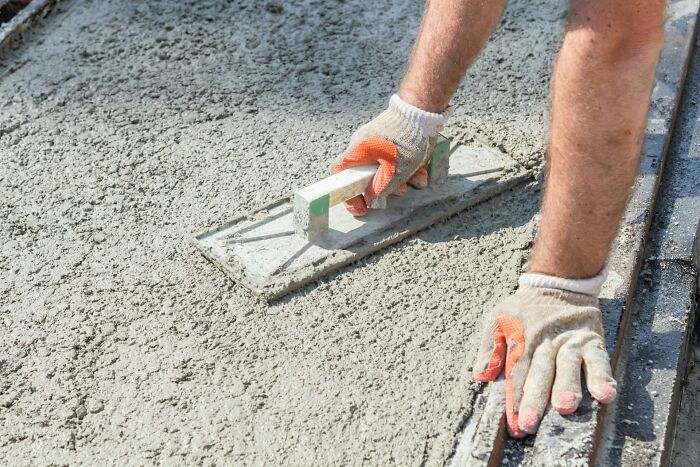Worker wearing gloves smoothing wet concrete with a hand float, illustrating work secrets from skilled trades like plumbing and construction.