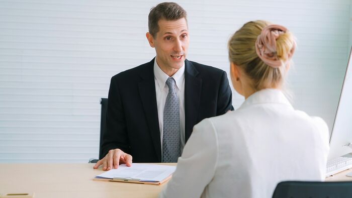 Two workers discuss unprofessional things done in an office setting during a formal meeting at a desk.