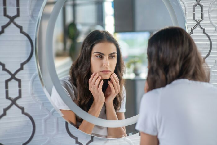 Young woman looking thoughtfully in the mirror, reflecting on signs a child was never loved properly in childhood.